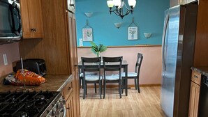 Een keuken met houten kasten, een roestvrijstalen koelkast, een gasfornuis en een eettafel met stoelen.