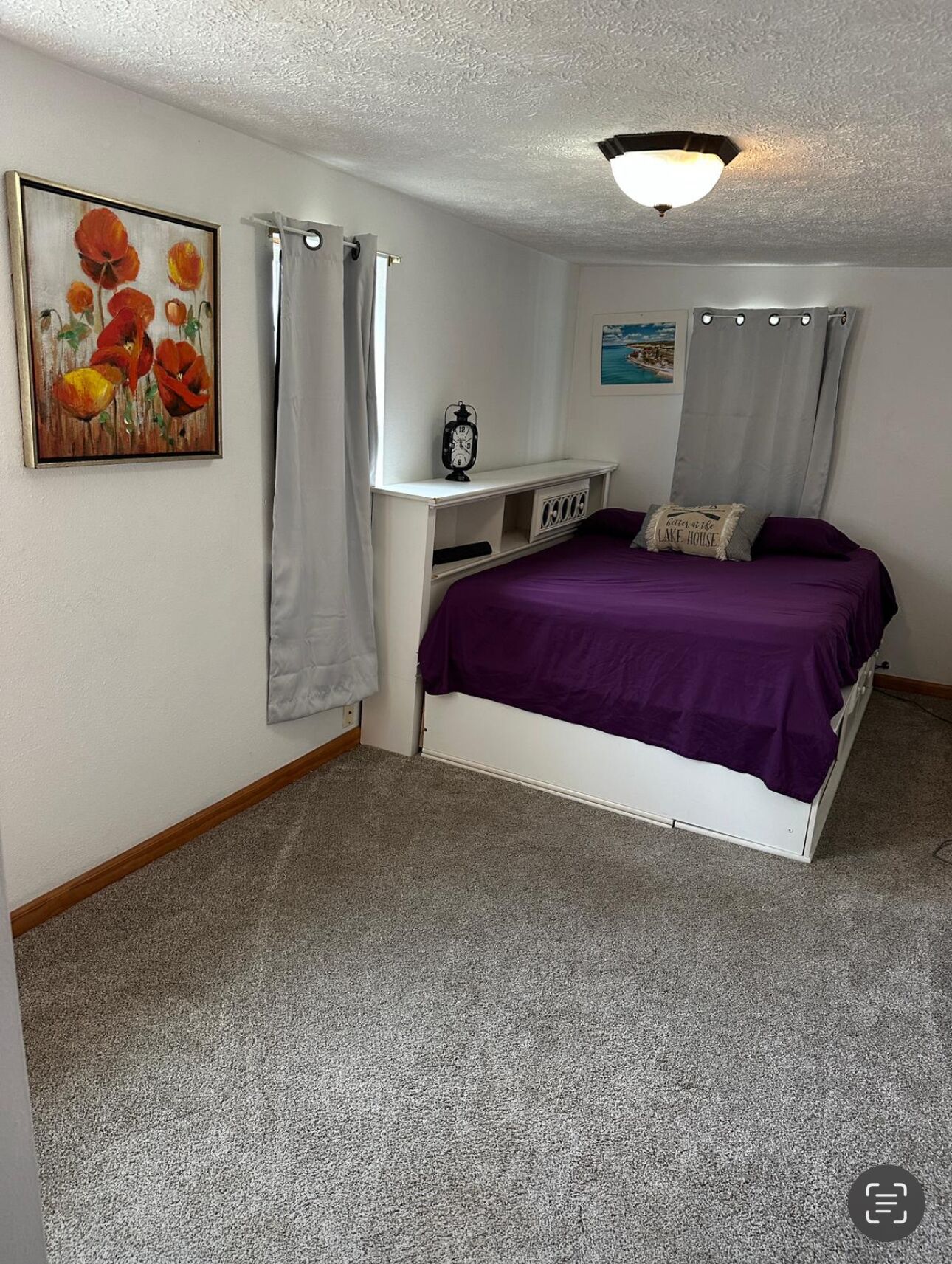 Une chambre à coucher avec un lit, une étagère sur laquelle se trouve une horloge, un tableau et une fenêtre avec des rideaux.