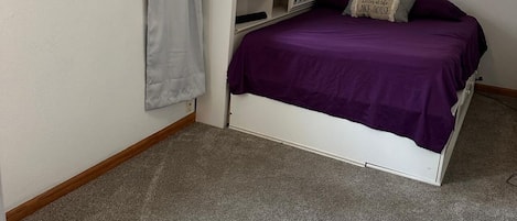 Une chambre à coucher avec un lit, une étagère sur laquelle se trouve une horloge, un tableau et une fenêtre avec des rideaux.