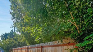 A patio with a fire pit table and two chairs, surrounded by a wooden fence and greenery. - Apt Getaway In Downtown Bozeman! (Bozeman)