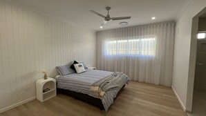 A bedroom with a bed, a ceiling fan, a window with curtains, and a door.