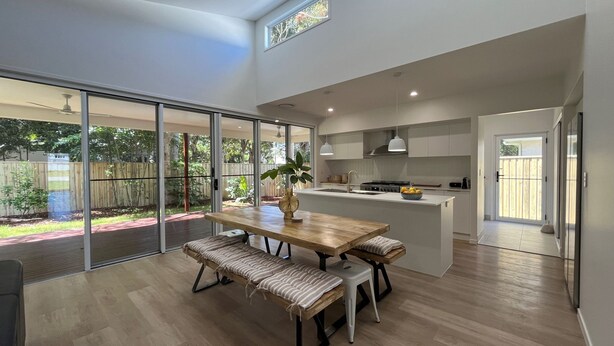 A modern kitchen with a central island, a dining area with benches, and large sliding glass doors leading to a backyard.