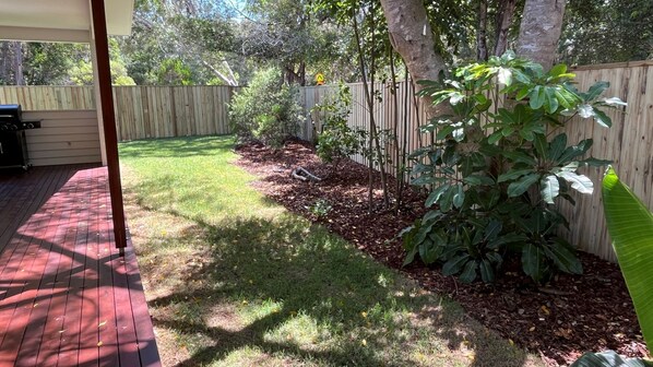 A backyard with a wooden deck, a grassy area, and a wooden fence.