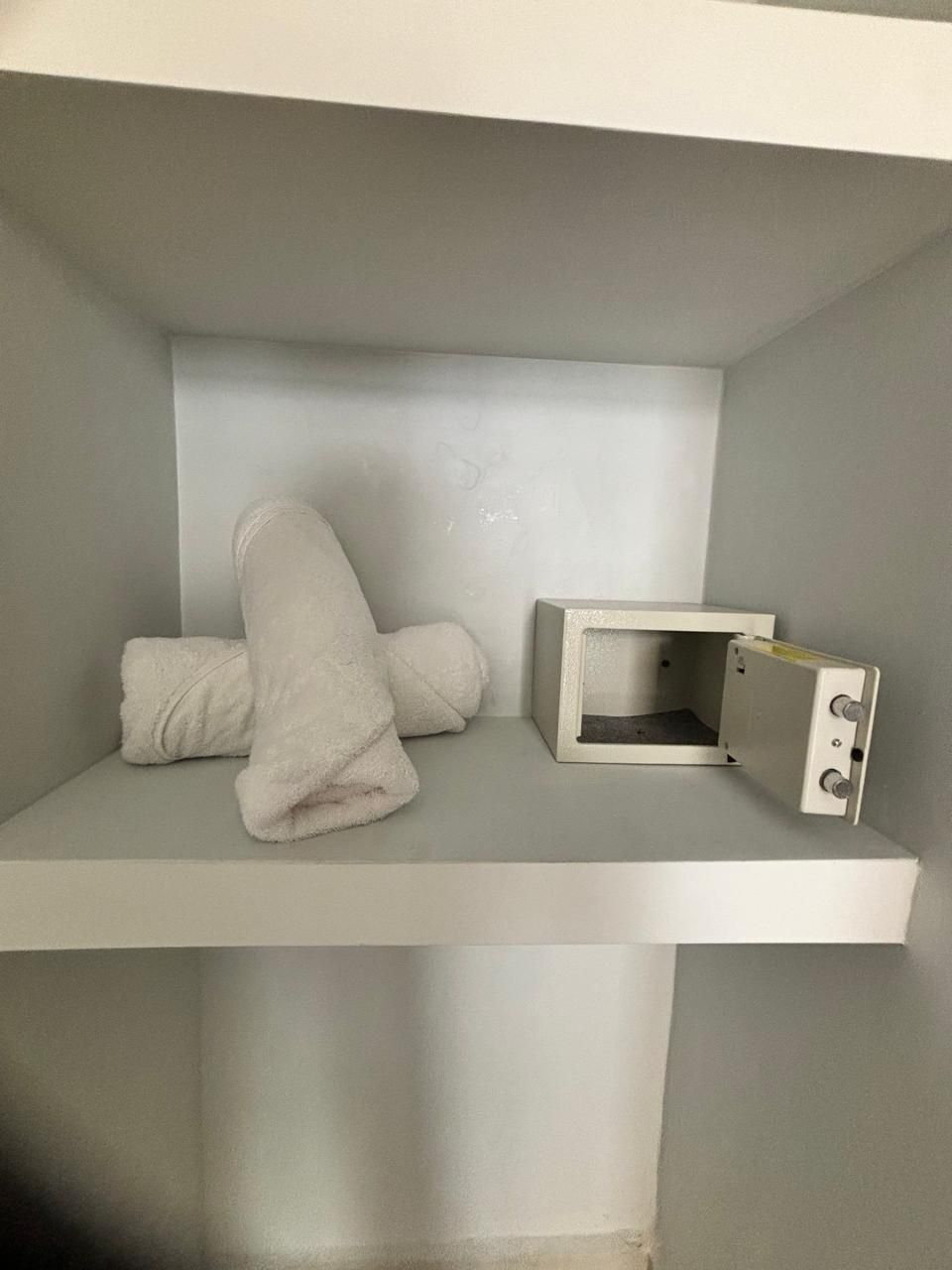 Un petit espace clos, avec une étagère blanche, une boîte blanche et une serviette blanche enroulée.