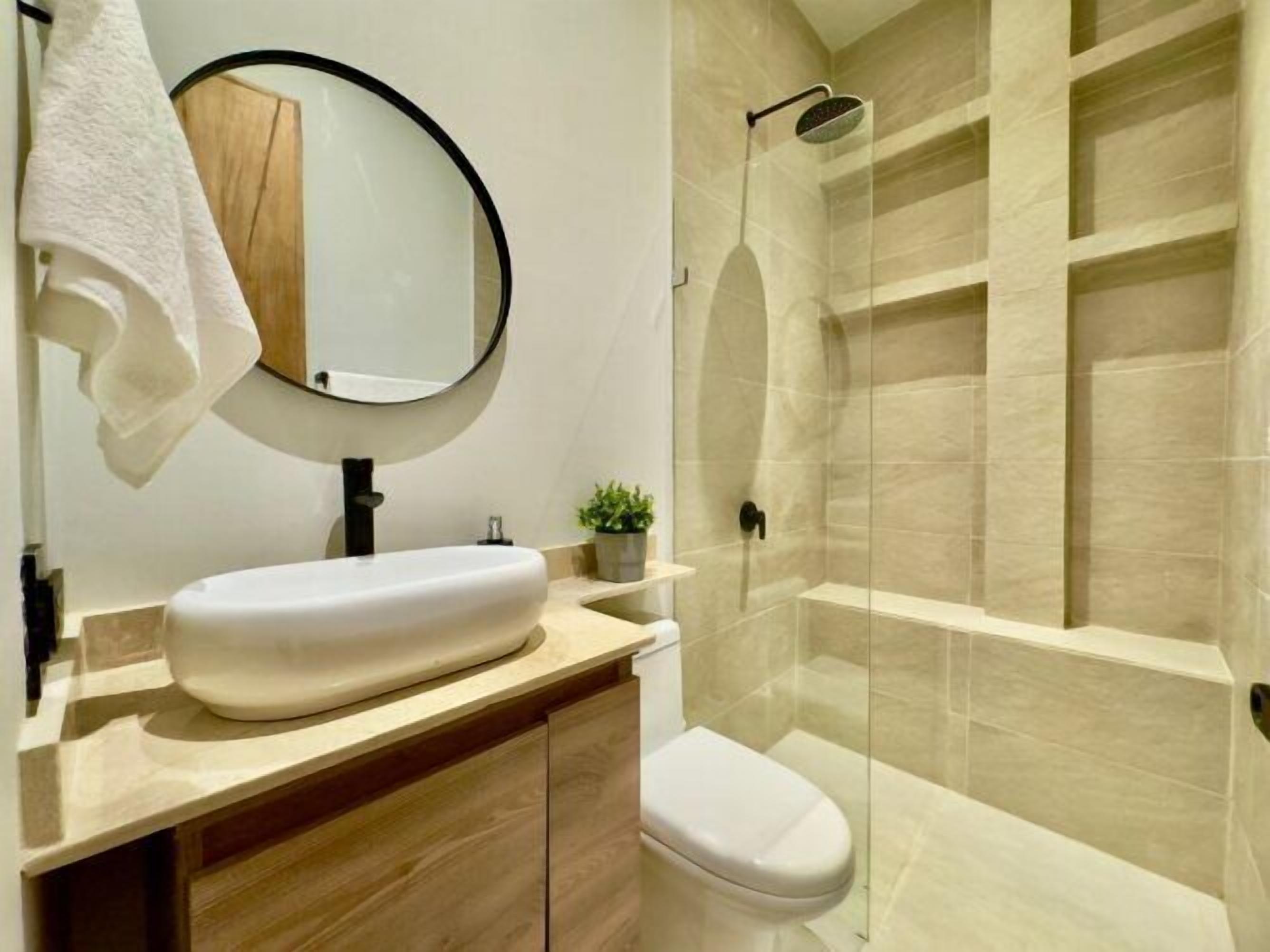 A modern bathroom with a white sink, a toilet, a mirror, and a glass-enclosed shower.