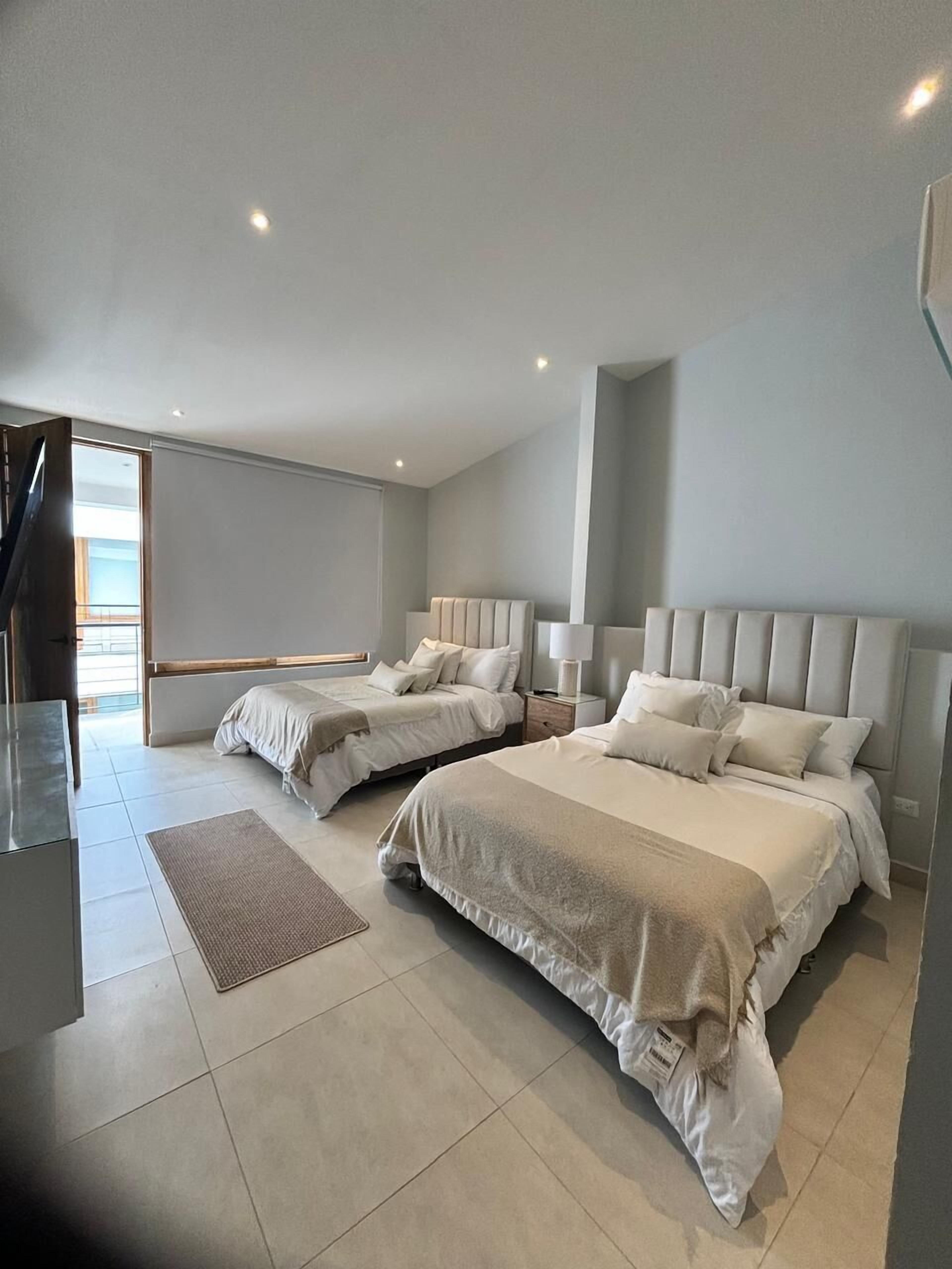 A modern bedroom with two beds, a large window, and a minimalist design.