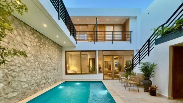 Una casa moderna con piscina, muro de piedra y zona de estar al aire libre.