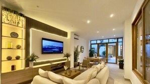 Una sala moderna con un televisor de pantalla plana grande montado en la pared, un sofá color beige, una mesa de centro y un comedor con mesa y sillas.