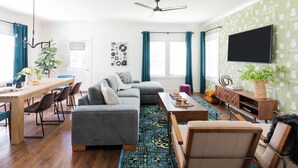 Ein modernes Wohnzimmer mit einer Eckcouch, einem Esstisch mit Stühlen, einem Couchtisch und einem flachbildfernseher an der Wand.