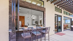 Un área de comedor al aire libre con pared de piedra, dos sillas de metal y una mesa con cuencos y una servilleta.