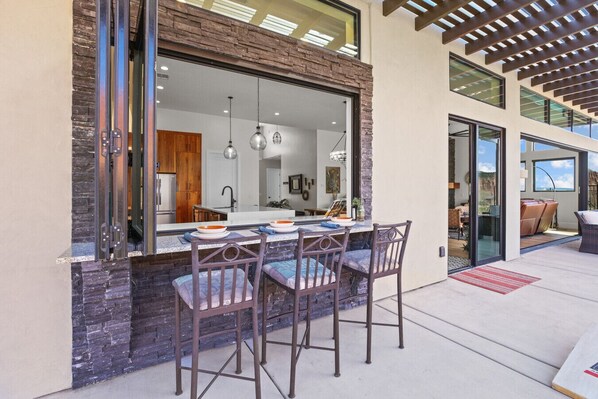 An outdoor dining area with a stone wall, two metal chairs, and a table with bowls and a napkin.