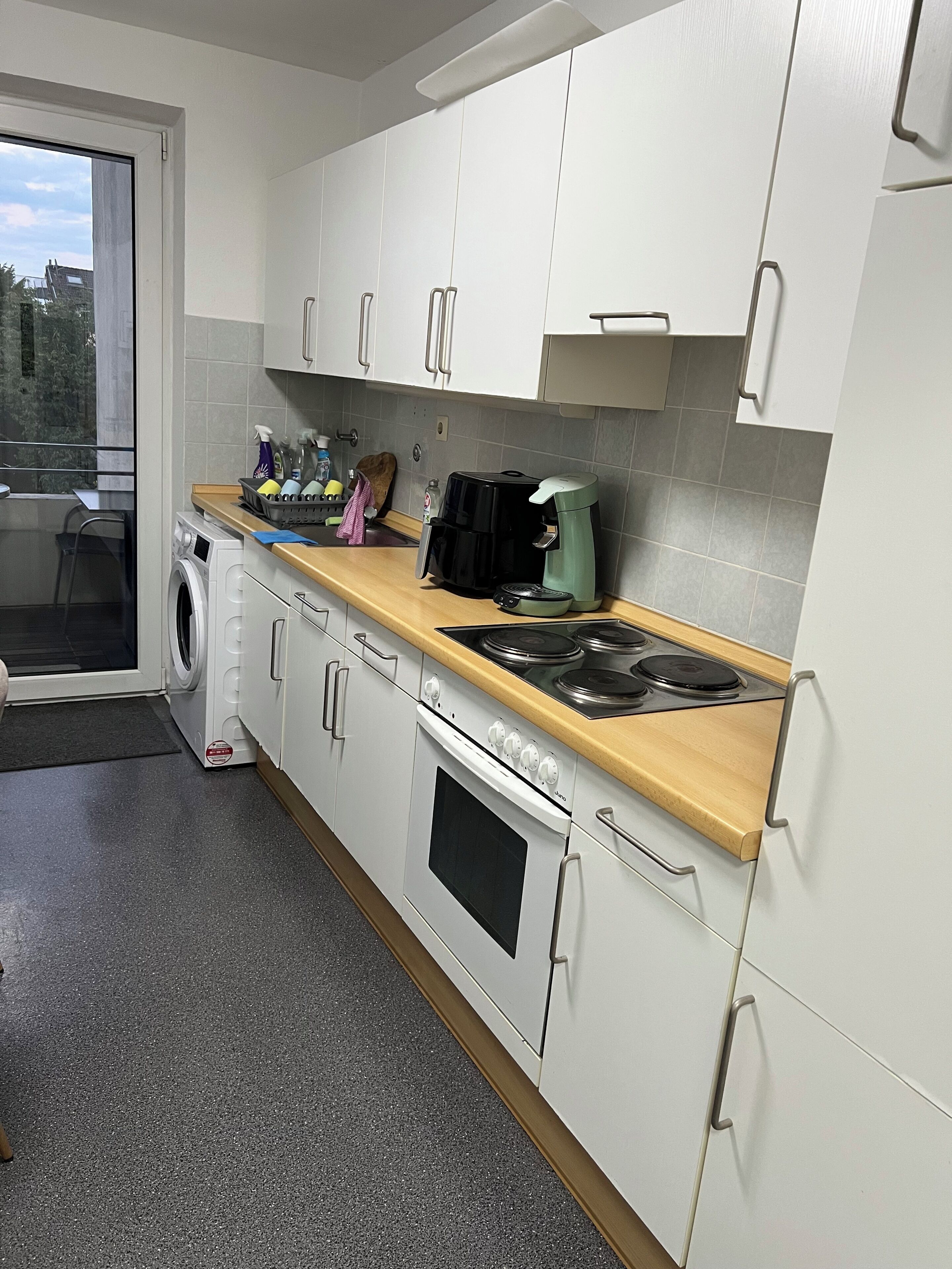 A kitchen with a washing machine, a coffee maker, and a stove.