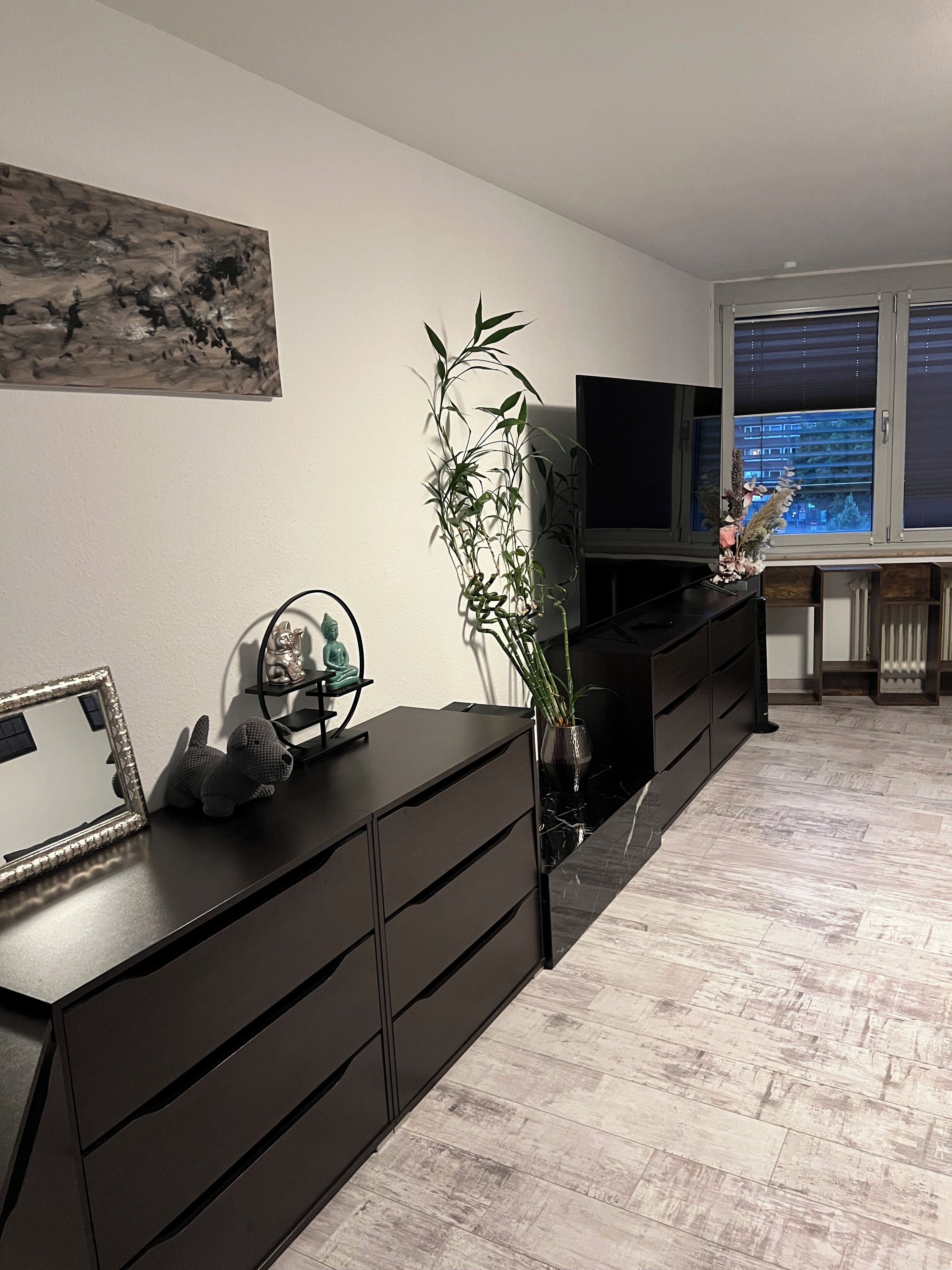 A modern living room with a large flat-screen TV, dark wooden furniture, a tall bamboo plant, and a painting on the wall.