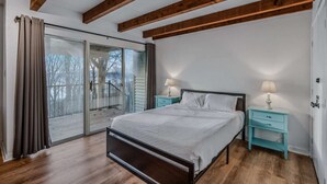 A bedroom with a bed, two nightstands, a sliding glass door, and wooden beams on the ceiling.