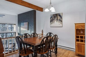A dining room with a wooden table and chairs, a brick accent wall, a painting, and a wooden cabinet. - Ski-In/Ski-Out Condo with Private Deck, Kingswood (Quechee)