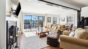 A spacious living room with a fireplace, a large window, and a balcony. - Condo with Fireplace, Sugar Hill (Quechee)