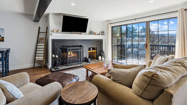 A living room with a fireplace, a television, and a large window. - Condo with Fireplace, Sugar Hill (Quechee)