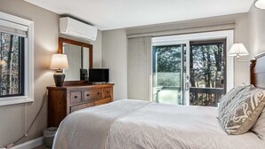 A bedroom with two beds, a dresser, a television, and a balcony with a view of trees. - Ski-In/Ski-Out Condo with Big Back Deck, Kingswood (Quechee)