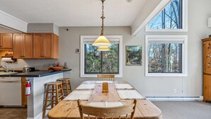 A spacious kitchen with wooden cabinets, a large island, and a dining area with a wooden table and chairs. - Ski-In/Ski-Out Condo with Big Back Deck, Kingswood (Quechee)
