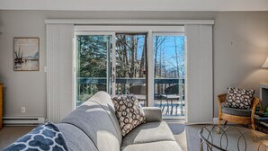 A living room with a grey sofa, patterned cushions, a wicker chair, and a glass table. - Ski-In/Ski-Out Condo with Big Back Deck, Kingswood (Quechee)