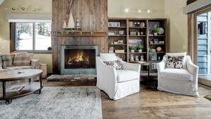 A cozy living room with a fireplace, white armchairs, a coffee table, and a bookshelf. - Townhouse, Mountain Views & Ski Access, Kingswood (Quechee)