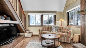 A living room with a sofa set, a coffee table, a TV, and a staircase. - Townhouse, Mountain Views & Ski Access, Kingswood (Quechee)
