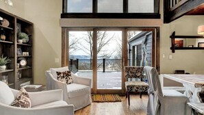 A spacious living area with a large sliding glass door leading to a balcony, wooden flooring, and a bookshelf filled with various items. - Townhouse, Mountain Views & Ski Access, Kingswood (Quechee)