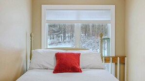 Ein Schlafzimmer mit einem Bett, einem Fenster mit Blick auf einen verschneiten Wald und einem Nachttisch mit einer grünen Lampe.