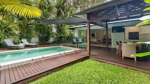A modern outdoor pool area with a wooden deck, lounge chairs, and a covered seating area.