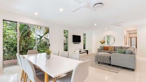 A modern living room with a dining area, large windows, and a ceiling fan.