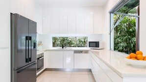 A modern kitchen with white cabinetry, a stainless steel refrigerator, a microwave, and a window with a view of greenery.