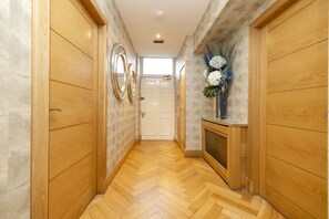 A hallway with wooden doors, a herringbone floor, and a decorative vase with flowers. - Argyl - Beautiful 3 Bedroom on York Place (Edinburgh)