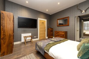 A bedroom with a bed, a television, a wooden wardrobe, a mirror, and a door.
