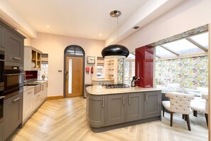 A modern kitchen with grey cabinets, a central island, and a dining area with white chairs. - Argyl - Beautiful 3 Bedroom on York Place (Edinburgh)