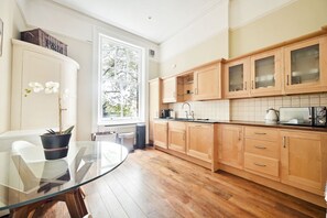 A modern kitchen with wooden cabinets, a glass table, and a potted plant.