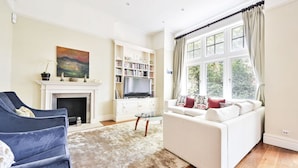 A living room with a fireplace, a television, a bookshelf, a sofa, and a large window.
