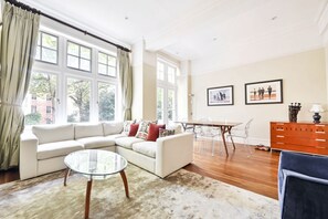 A living room with a sofa, glass coffee table, dining table, chairs, and a dresser.