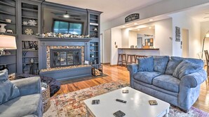 A modern living room with a fireplace, a sofa, a coffee table, and a dining area. - Chain of Lakes Escape with Hot Tub & River Access! (Bellaire)