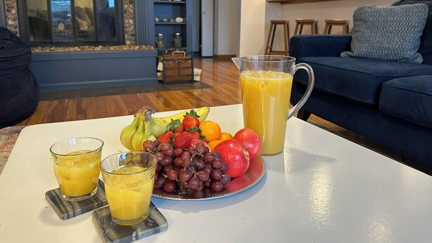 A dining area with a table set for breakfast, including fruits, juice, and glasses. - Chain of Lakes Escape with Hot Tub & River Access! (Bellaire)