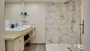 Uma casa de banho moderna com chuveiro de mármore, sanita com divisória de vidro e toucador com lavatório e espelho.