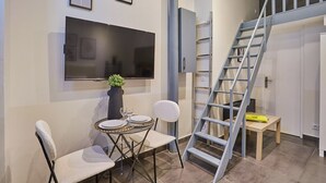 Uma área de refeições com uma mesa posta para dois, uma televisão na parede e uma escada com corrimão de metal.