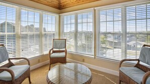A sunroom with large windows, wicker furniture, and a glass table.