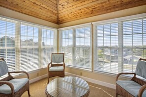 A sunroom with large windows, wicker furniture, and a glass table.