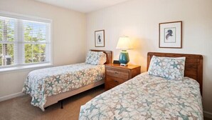 A bedroom with two beds, a nightstand, a lamp, and a window with blinds.