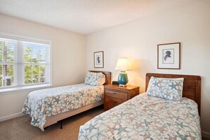 A bedroom with two beds, a nightstand, a lamp, and a window with blinds.