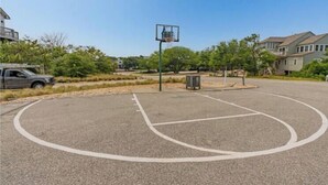 An outdoor basketball court with a hoop, surrounded by trees and residential buildings.