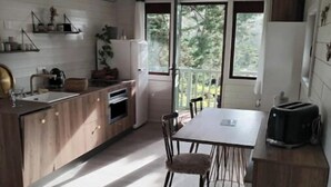 A modern kitchen with wooden cabinets, a dining table, and a large window overlooking a garden.