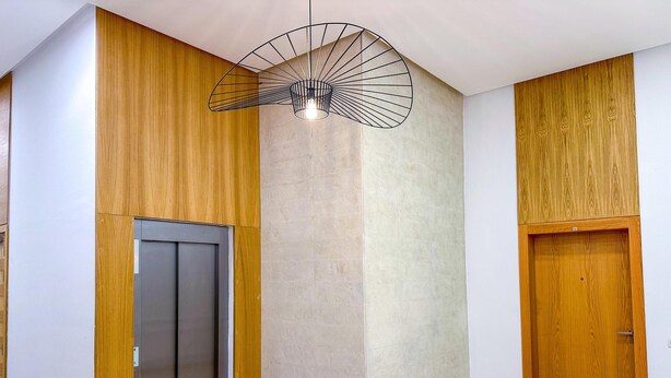 A modern interior with a wooden panel wall, a central light fixture, an elevator, and a wooden door. - Luxury studio & Centric flat  (Casablanca)
