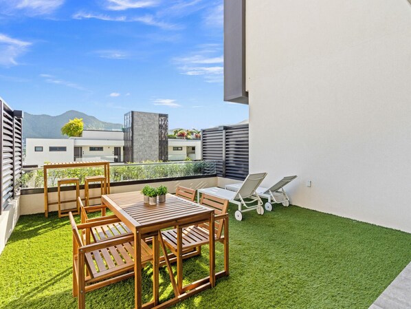 A rooftop terrace with a wooden table and chairs, a small garden, and a view of buildings and mountains. - B206 - Magnificent 1 bedroom with terrace (Cole Bay)