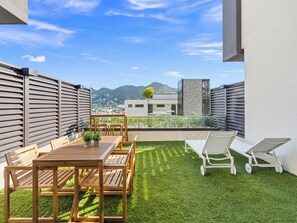 A rooftop terrace with a wooden table and chairs, a small garden, and a view of a cityscape and mountains in the background. - B206 - Magnificent 1 bedroom with terrace (Cole Bay)